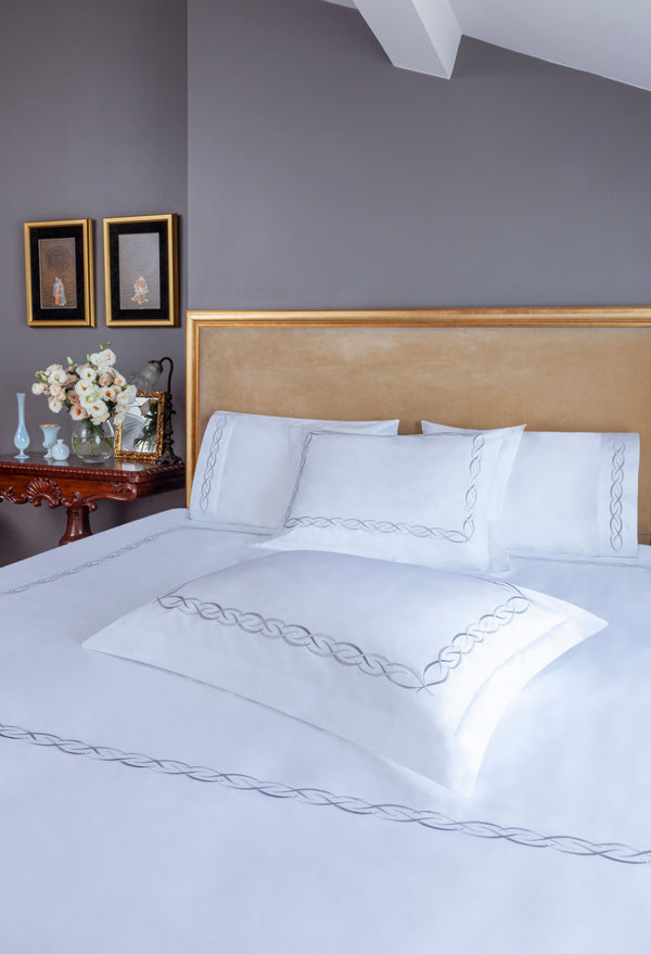 Ava Duvet Cover Set in white Egyptian cotton with elegant linked loop embroidery – flanged shams and pillowcases on bed, styled in luxury bedroom.