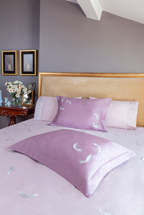 Feathers Duvet Cover Set in light rose Egyptian cotton with feather embroidery – flanged shams and pillowcases on bed, styled in luxury bedroom.