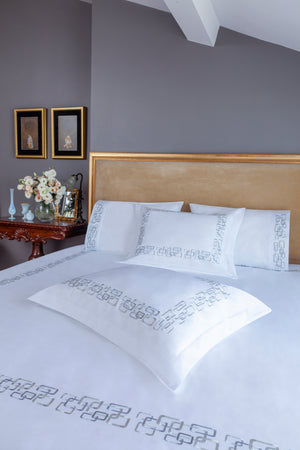 Geometric Duvet Cover Set in white Egyptian cotton with geometric embroidery – flanged shams and pillowcases on bed, styled in luxury bedroom.