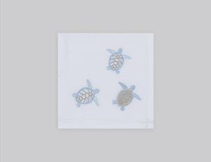 White linen cocktail napkin embroidered with ice blue sea turtles, 100% European linen, handcrafted by Plein Soleil.