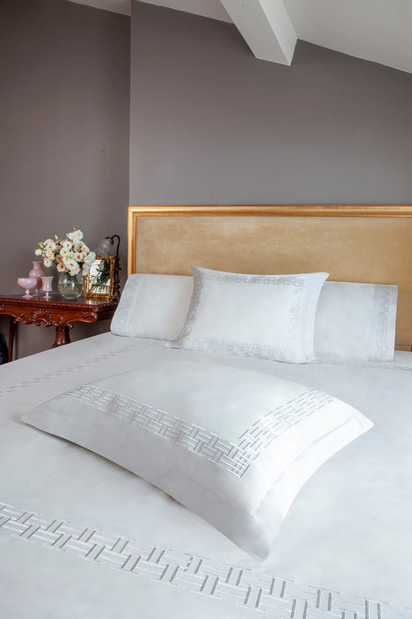 Versa Duvet Cover Set in white Egyptian cotton with geometric embroidery – flanged shams and pillowcases on bed, styled in luxury bedroom.