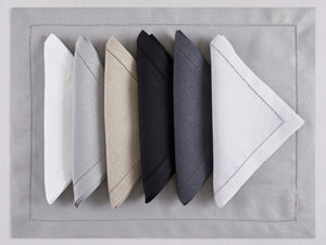 Assorted hemstitch linen napkins and placemats in white, gray, natural beige, black, anthracite, and ivory—100% European linen, handcrafted by Plein Soleil.