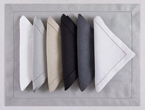 Assorted hemstitch linen napkins and placemats in white, gray, natural beige, black, anthracite, and ivory—100% European linen, handcrafted by Plein Soleil.