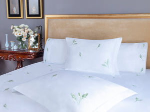 Lily of the Valley Duvet Cover Set in white Egyptian cotton with lily embroidery – flanged shams and pillowcases on bed, styled in luxury bedroom.