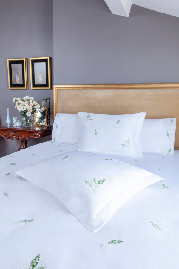 Lily of the Valley Duvet Cover Set in white Egyptian cotton with lily embroidery – flanged shams and pillowcases on bed, styled in luxury bedroom.