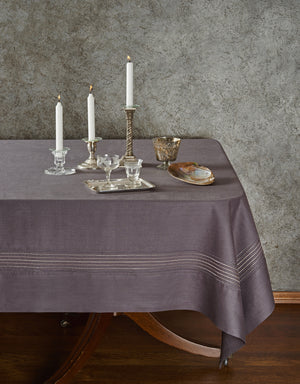 Table setting with a gray tablecloth, candles, and glassware against a textured wall.