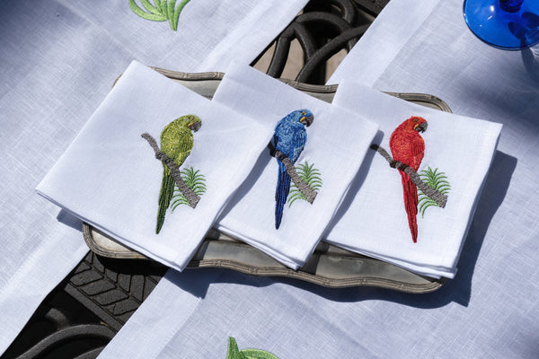 Set of embroidered napkins with parrot designs on a table.