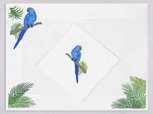 White linen placemat and napkin set embroidered with a blue parrot and green palm trees, 100% European linen, handcrafted by Plein Soleil.