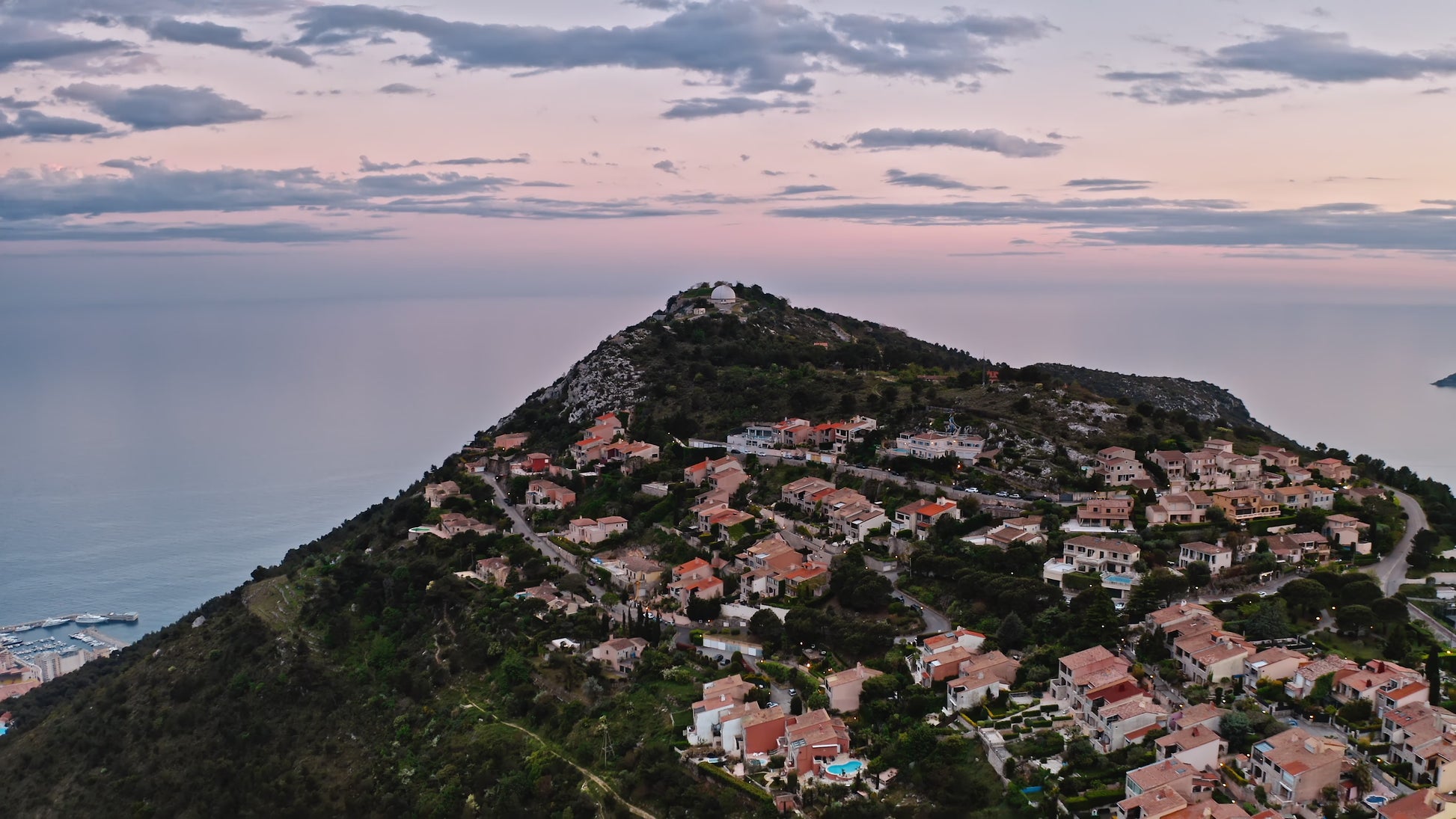 Aerial view of a hillside village on the French Riviera at sunset, with pastel skies and Mediterranean architecture — evoking the essence of Plein Soleil’s elegant coastal inspiration.