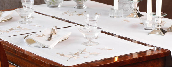 Dining table setting with placemats, cutlery, and glasses on a wooden table.