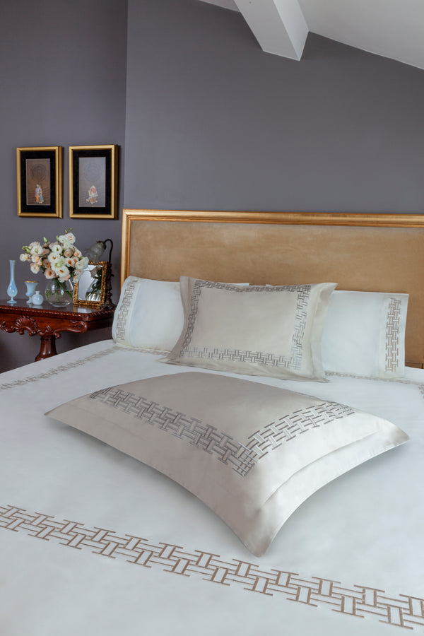 Versa Duvet Cover Set in ivory Egyptian cotton with geometric embroidery – flanged shams and pillowcases on bed, styled in luxury bedroom.