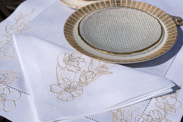 White napkin with gold floral embroidery on a table setting with a gold-rimmed plate.