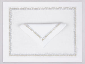 White linen placemat and napkin set embroidered with gold and silver zig zag motif border, 100% European linen, handcrafted by Plein Soleil.